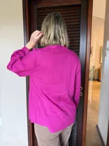 Camisa de manga larga en color fucsia, con cuello mao y cierre frontal de botones. Presenta detalles de alforzas verticales en el frente y puños abotonados.