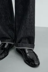 Mocasín de vestir negro, con acabado liso y brillante, puntera cuadrada y detalle de antifaz en el empeine. Posee suela fina y tacón bajo.