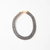 Collar tipo gargantilla rígida de diseño tubular, recubierto con cristales brillantes en tono gris oscuro, con cierre y cadena de extensión en metal dorado.