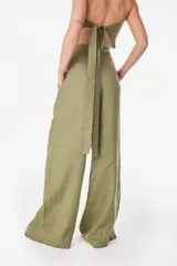 Pantalón de lino blanco de corte ancho y fluido, con cintura alta que incorpora una sobrepretina ancha desmontable con pliegues horizontales.