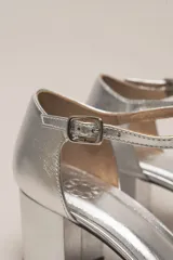 Sandalia de cuero color bordó, con acabado charolado, punta fina y tacón cuadrado de 5 cm. Presenta una tira en forma de T sobre el empeine y una correa con hebilla alrededor del tobillo.