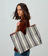 Cartera shopper de algodón con diseño a rayas en tonos neutros y detalles de ribetes y asas de hombro en PU marrón. Cuenta con una abertura central pronunciada y gran capacidad de almacenamiento.