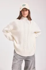 Sweater de punto negro con diseño de trenzas verticales, cuello alto y corte holgado de estilo oversize.