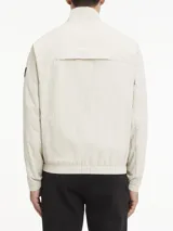 Campera Calvin Klein color beige claro, confeccionada en nailon arrugado reciclado. Tiene cuello alto, puños y bajo elásticos, cierre con cremallera, bolsillos con cremallera en la cintura, abertura de ventilación en la espalda, forro de poliéster reciclado e insignia con el logo de goma de Calvin Klein en la manga.