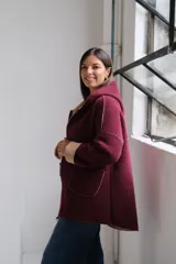 Tapado de paño bordó con interior en color beige, diseño con capucha, cierre frontal y bolsillos laterales. Presenta costuras visibles y puños vueltos que dejan ver el contraste de color.