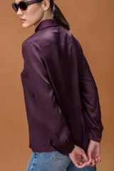 Camisa de seda color violeta oscuro, con cuello clásico, cierre frontal de botones y mangas largas con puños abotonados.