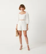 Blusa corta blanca de algodón con escote cuadrado, manga larga abullonada con bordados, y látex en la espalda.