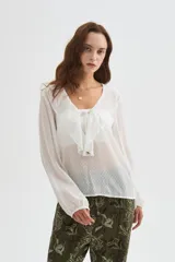 Blusa blanca de poliéster con cuello en V, volados frontales y mangas largas con elástico en los puños.