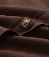 Camisa tipo overshirt de Ashua confeccionada en suede sintético color marrón. Presenta cuello clásico, cierre frontal con botones, mangas largas con puños abotonados y dos bolsillos frontales aplicados.