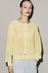 Chaqueta de punto rústico color amarillo claro, con cuello redondo, manga larga y cierre frontal con botones nacarados.