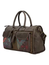 Cartera de mano marrón de estilo bohemio con detalles en tela étnica tipo tapicería bajo los bolsillos frontales con solapa. Cuenta con doble asa fija, correa ajustable y desmontable, cierre superior y llavero colgante con borla y cuentas decorativas.
