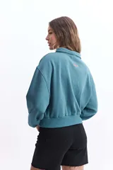 Buzo de felpa color crudo con cuello alto, cierre metálico y bordado de un corazón con rayos en el pecho.