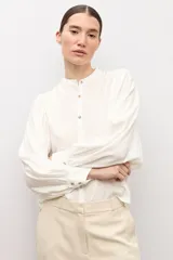 Camisa blanca de corte recto con cuello mao, cierre frontal de botones y mangas largas abullonadas con puños ajustados.