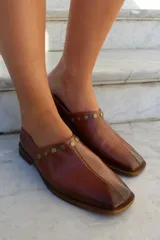 Zapato de cuero vacuno color bordó, con diseño de punta cuadrada y detalle de tachas metálicas planas en el borde superior. Presenta un taco geométrico bajo y costura central en el empeine.