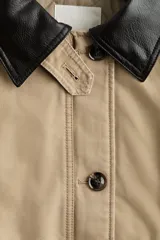 Campera levemente acolchada en lona de algodón gruesa color beige, con cuello y puños vueltos de efecto cuero marrón oscuro. Presenta cierre frontal con botones, solapa rompevientos, bolsillos delanteros de parche con solapa y bolsillos calientamanos.
