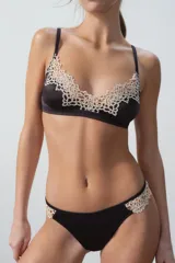 Conjunto de lencería compuesto por un corpiño triangular y una bombacha tipo colaless, ambos en color negro con detalles de encaje floral en tono crema en los bordes.