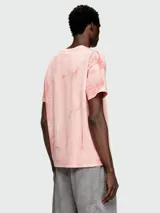Remera de manga corta, cuello redondo y calce holgado, color rosa pálido con un efecto de teñido o estampado que simula grietas o craquelado en tonos más oscuros de rosa/naranja.