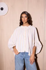 Camisa holgada de algodón con cuello alto y mangas anchas, confeccionada en Italia. Presenta un estampado de rayas verticales finas en tonos beige, blanco, amarillo, rojo y azul.