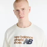 Remera de manga corta New Balance de color blanco marfil, con diseño de cuello redondo y estampa frontal que combina texto en tonos marrón y azul marino con el logotipo clásico de la marca.