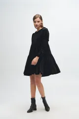 Vestido corto de terciopelo negro con diseño de volados escalonados, mangas largas con detalles de fruncidos y cuello redondo con volado pequeño.