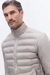Campera puffer de nylon color beige, con diseño minimalista, cuello alto, cierre frontal y puños elásticos. Presenta logo de la marca bordado en el pecho.