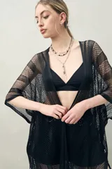 Poncho negro de tejido calado con flecos en el ruedo.