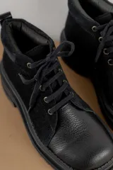 Borcegos de punta cuadrada con diseño acordonado, combinando paneles de cuero texturizado y gamuza en tonos marrones. Presentan una suela track gruesa de goma negra y cordones negros.