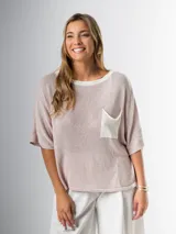 Remera tejida color crema con cuello redondo y bolsillo frontal verde.