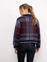 Campera de punto con diseño a cuadros tartán en tonos marrones y beige. Presenta un corte oversize, cierre frontal con cremallera, cuello tipo babero con volados y mangas largas con puños ajustados.