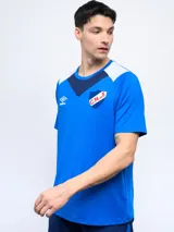 Remera de entrenamiento Umbro del Club Nacional de Football, color azul con detalles en blanco y azul marino en los hombros y cuello. Presenta el logo de la marca y el escudo del club en el pecho.