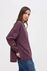 Buzo oversize de felpa con friza, color bordó, con cuello redondo, mangas largas con cortes decorativos y tajos laterales en el ruedo. Presenta un bordado de la marca en una de las mangas.
