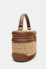 Bolso tipo vanity combinado en rafia y efecto cuero marrón, con cuerpo de tejido trenzado, detalles de pespuntes, asa de mano superior y cierre de cremallera.