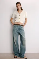 Chaqueta corta de punto texturizado color blanco roto, con escote en V, manga corta y cierre frontal con tres botones metálicos dorados en forma de estrella de mar.