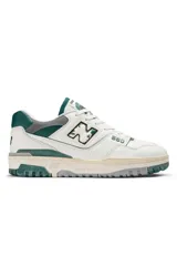 Championes New Balance modelo 550, de diseño retro inspirado en el básquetbol. Presenta una base de cuero blanco con detalles en verde oscuro y gris, incluyendo el logo 'N' con efecto desgastado y suela de goma con acabado envejecido.