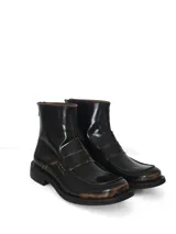 Botín de cuero negro con acabado brillante y efecto desgastado en tonos marrones en la puntera y detalles. Presenta un diseño tipo mocasín con antifaz en el empeine, caña media y cierre posterior.