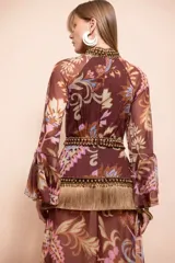 Vestido largo de mujer estilo boho en tono marrón, con estampado paisley y floral, cuello alto, abertura frontal en el escote y mangas largas abullonadas. Cuenta con detalles de aplicaciones de pedrería y flecos en la cintura, y falda larga con tajo lateral.