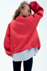 Cazadora roja de satén con cuello subido, manga larga con hombreras, bolsillos delanteros con cierre, bajo ajustable con cordón elástico y cierre frontal de cremallera metálica.