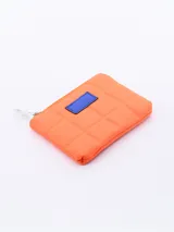 Monedero de diseño acolchado en color verde, con cierre metálico superior y detalle de parche rectangular en color amarillo en el frente.