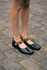 Ballerinas de cuero negro con punta cuadrada y tira de gamuza marrón en el empeine decorada con tachas metálicas plateadas.