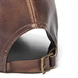 Gorra tipo béisbol confeccionada en cuero sintético color marrón con efecto desgastado y costuras decorativas en contraste.