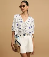 Blusa de mangas abullonadas cortas, confeccionada en Viscolino con 15% de Lino, con cuello v con lazo y estampa de accesorios de playa.