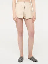 Short de cuerina color beige claro, con diseño de cruce frontal que simula un pareo o falda-pantalón, cierre oculto y un botón metálico decorativo en la cintura.