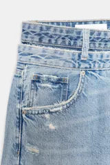 Jeans de tiro medio, color azul claro, con doble cinturilla y trabillas. Presenta cinco bolsillos, detalles de rotos y cierre frontal con cremallera y botones.