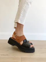Sandalias de cuero color negro y camel, con plataforma track y hebilla ajustable.