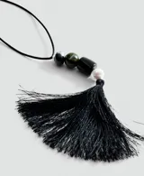 Collar largo con cordón negro y colgante compuesto por cuentas de diferentes materiales y colores (verde, negro y perla) rematado con una borla de flecos negros.