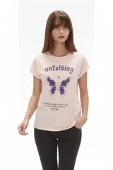 Remera rosada de manga corta, con diseño holgado y estampado frontal de mariposa y texto en tonos morados.