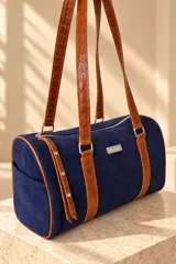 Cartera tipo baulito de cuero color marrón tostado, con doble asa larga de hombro, cierre superior y detalle de placa metálica con el logo de la marca en el centro.