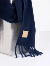 Bufanda de tejido suave en color rosado, con diseño liso y terminaciones con flecos en los extremos. Incluye una etiqueta de cuero sintético con el logo de la marca en uno de los bordes.