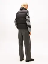 Chaleco acolchado de corte regular, confeccionado en poliéster reciclado. Presenta cuello alto con cierre de botones a presión, cierre frontal de cremallera oculto y diseño sin mangas. Incluye detalles distintivos y logo de la marca.