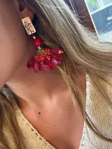 Aros colgantes con base rectangular dorada con textura, seguidos de una esfera roja y un diseño colgante con forma de abanico con cuentas rojas y detalles dorados.